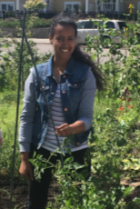 woman in jean vest standing in a vegetable garen holding a trellis and smiling